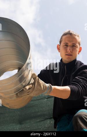 Low angel of concentrated man working passing his colleague a metalic pipe in a construction site Stock Photo