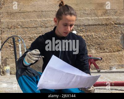 Young man working and running a construction site while holding the blueprints and a pencil in his hand Stock Photo