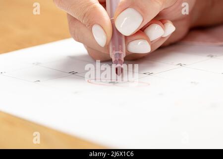 female hand marking with a red pen on a calendar circles the day, deadline concept Stock Photo