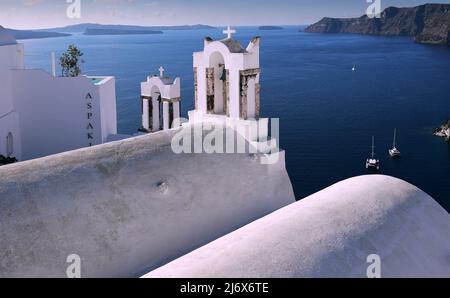 Oia, Santorini, Greek Islands, Greece - Pretty Greek Orthodox church with bell tower on clifftop in dazzling bright sunslight overlooking the sea Stock Photo