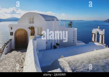 Oia, Santorini, Greek Islands, Greece - Pretty shop perched on clifftop next to church with bell tower overlooking sea in dazzling bright sunslight Stock Photo