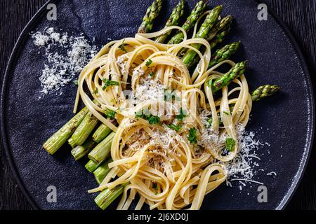 roasted asparagus spears with spaghetti sprinkled with shredded pecorino cheese and parsley on black plate , flat lay, close-up, macro Stock Photo