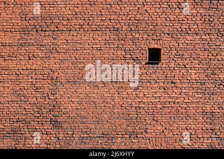 A single window in a huge brick wall. The sun illuminates the wall Stock Photo