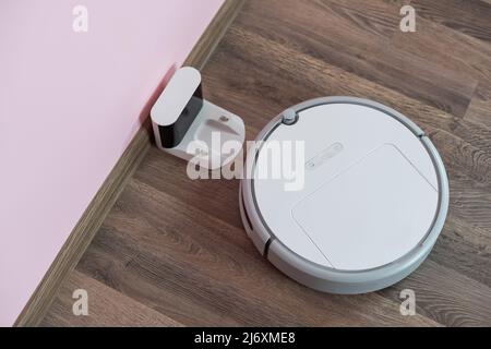 Robotic vacuum cleaner on laminate wood floor charging from base station. Smart cleaning technology. robot vacuum cleaner return to charging at dock Stock Photo