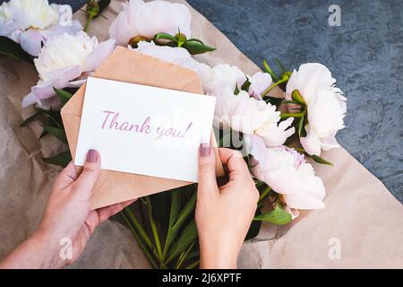 Thank you card in hands, message, envelope, pink peony flowers bouquet Stock Photo