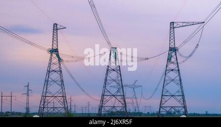 Industrial background group silhouette of transmission towers or power tower, electricity pylon, steel lattice tower at purplr sunset. Texture of high Stock Photo