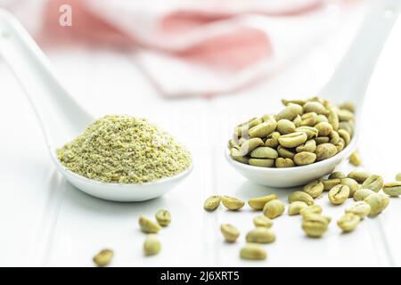 Ground green coffee and unroasted coffee beans on a white table. Stock Photo