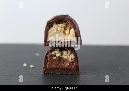 two chocolate candies in a cut with a filling of praline mousse with peanuts hazelnuts on a gray background. Dessert pleasure day of chocolate sweets. Stock Photo