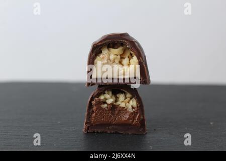 two chocolate candies in a cut with a filling of praline mousse with peanuts hazelnuts on a gray background. Dessert pleasure day of chocolate sweets. Stock Photo