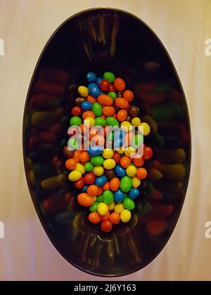 A lot of multicolored dragees poured into a plate, delicious round candies in the glaze of many colors. Dragee in a plate in honor of the holiday Stock Photo