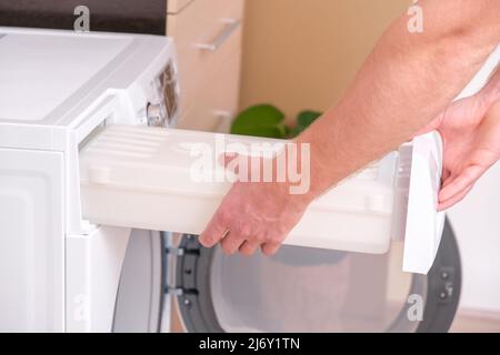 A man takes out a container from the dryer to collect water squeezed out of wet laundry. Stock Photo