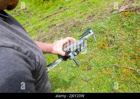 young man holding DJI Mavic Pro drone hovering against green grass bushes background Stock Photo
