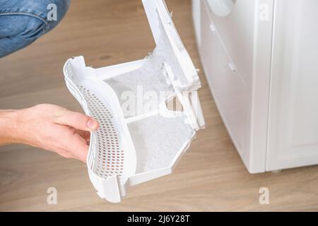 A man takes a lint filter out of the dryer and cleans it from dust, lint, hair, wool. Stock Photo