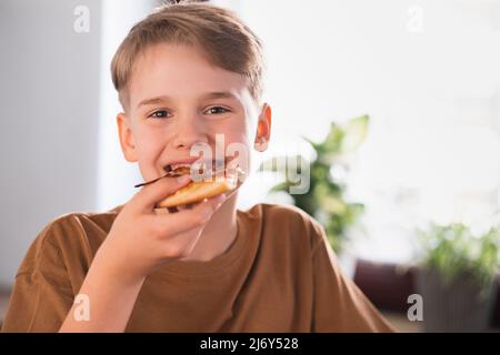 Satisfied boy enjoys eating delicious pizza in the kitchen at home. Stock Photo