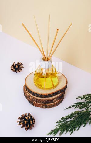 Glass bottle of aroma diffuser and pine cones on wooden stand on a white table. Close up. Stock Photo