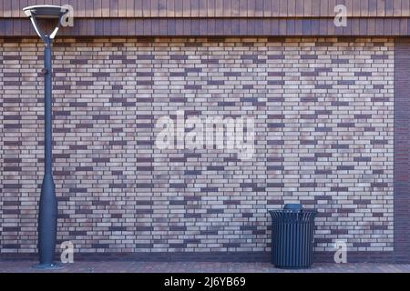 Dark brick wall pattern with chaotic masonry order. Background texture modern stone wall with lamp post and street trash can Stock Photo