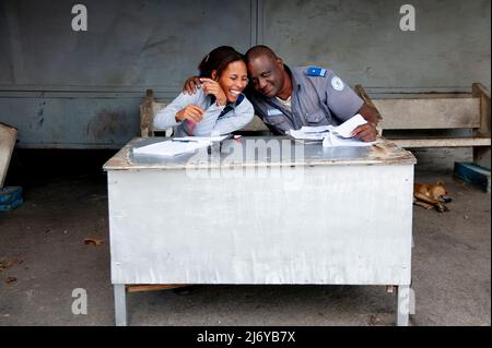 Cuban man and woman security office co-workers laugh together while working as a street dog sleeps on the ground in Havana, Cuba. Stock Photo