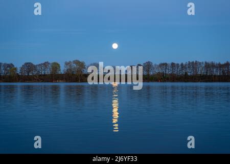 Moonrise over a tranquil lake landscape view. Bright shining moon reflected on the water surface. Idyllic evening in the nature. Night environment Stock Photo