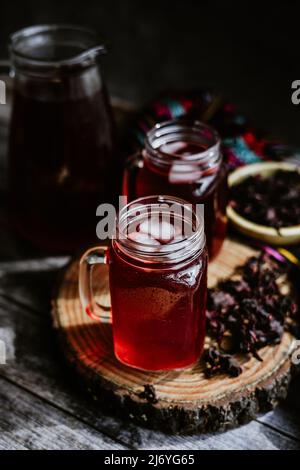 Agua de Jamaica or roselle mocktail drink, summer beverage in mexico with ice and dry hibiscus petals on table background Stock Photo