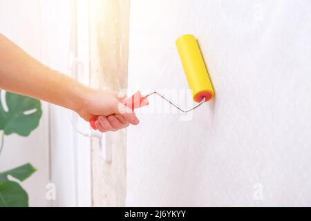 A man rolls out a canvas of white wallpaper with a suture wallpaper yellow roller. Removing air bubbles and glue from under the wallpaper. Wallpapering. Repair of a room, apartment, house. Stock Photo