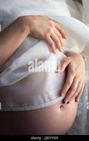 Close-up and detail shot of a pregnant woman's abdomen, whose bulging abdomen is covered with a delicate cloth Stock Photo