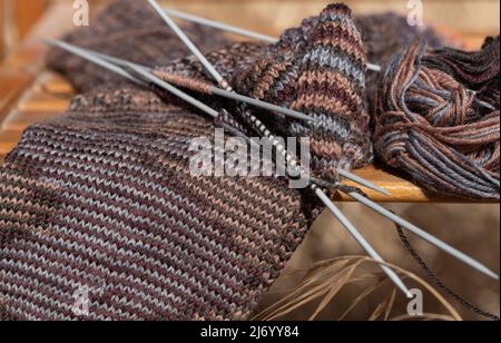 Close-up of a handwork that is not yet finished. Unfinished socks with knitting needles lying outdoors. Stock Photo