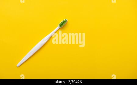 White plastic toothbrush on bright yellow background as flat lay, top view, space for text Stock Photo