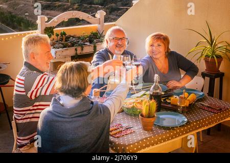 Mature adult friends enjoy clinking with wine at the table. Happy retired people have fun toasting with glasses. Retired men and women celebrate and l Stock Photo