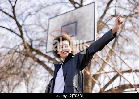 low angle view of happy african american woman standing with outstretched hand on basketball outdoor court Stock Photo