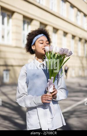 joyful african american woman looking at tulips on street Stock Photo