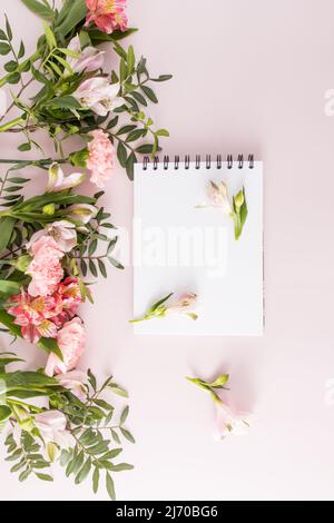 vertical top view of the blank white sheets of the notebook. pink pastel background with spring flowers. An empty layout for text Stock Photo