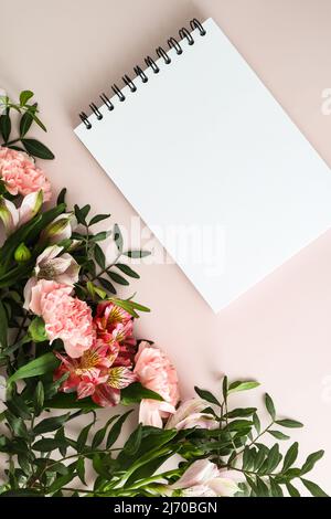 vertical top view of the blank white sheets of the notebook. pink pastel background with spring flowers. An empty layout for text Stock Photo