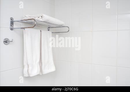Interior of bathroom with iron shelf and soft towels. White tiles with minimal composition in bathroom. Stock Photo