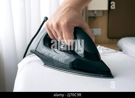 Close-up of hand with black iron on board during ironing Stock Photo