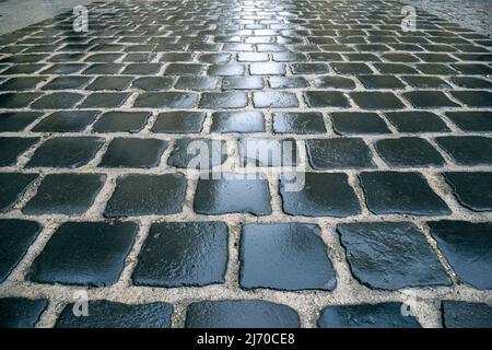 Old wet stone sidewalk or pavement as texture or background. Perspective of a wet road in a town Stock Photo