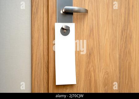 Paper blank label as mockup on door handle at the hotel. Wooden pine door and white long sheet with space for text. Stock Photo