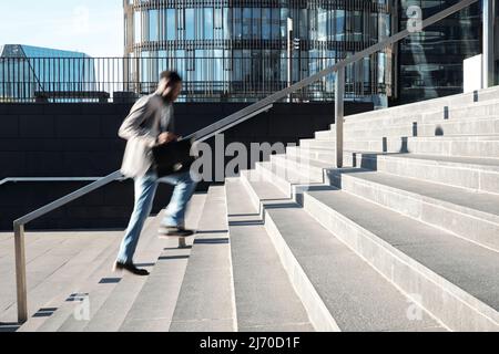 African American white collar worker running up the steps towards modern business center, blurred motion Stock Photo