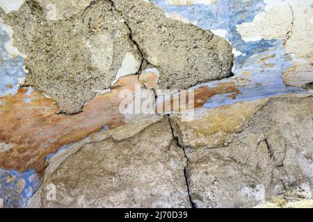 Big deep winding crack on old plastered colorful wall. Remains of colored plaster. Numerous layers of paint. Close up. Selective focus. Stock Photo