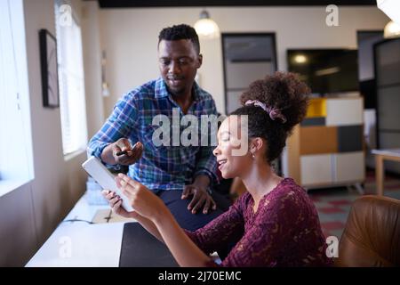 Two diverse colleagues discuss notes in their creative office Stock Photo