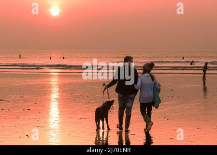 Dog walkers walking on Fistral Beach during an intense sunset in Newquay in Cornwall in the UK. Stock Photo