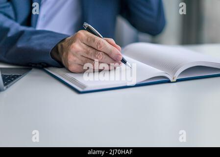 Senior business professional writing ideas on diary, Businessman making notes and planning strategy at desk, He is working in corporate office. Stock Photo