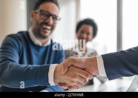 Happy business professionals shaking hands in meeting, Entrepreneurs congratulating over successful deal, They are sitting in corporate office. Stock Photo