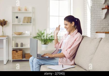 Woman waving in front of laptop webcam welcoming conference participants during online meeting. Stock Photo