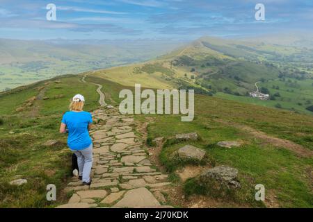A woman walking a paved path at the top of Mam Tor Castleton in the High Peak of Derbyshire, Peak District National Park, England, UK Stock Photo