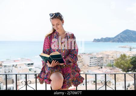 young woman on balcony with book and sea view Stock Photo
