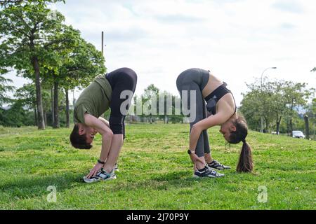 Young sporty couple stretching bending all the body outdoors on the grass. Stock Photo