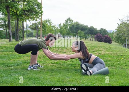 Personal trainer helping young woman doing splits and stretching exercises. Stock Photo