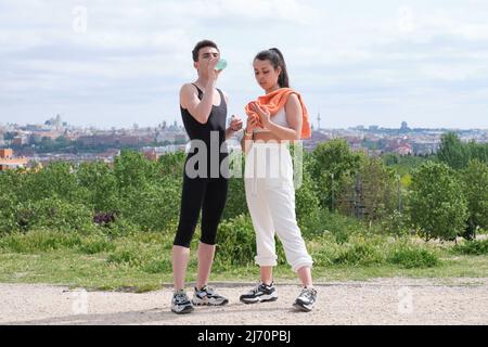 Young sporty couple drinking water and towel off sweat standing in a park. Stock Photo