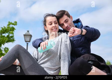 Happy young sport couple looking at smartwatch while sitting at a park. Stock Photo