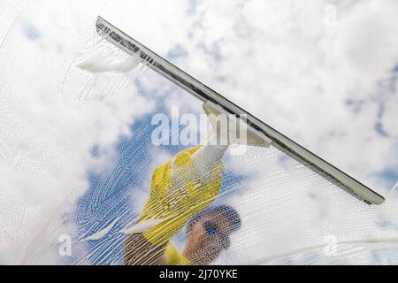 Window cleaner using a squeegee to wash a window. Stock Photo